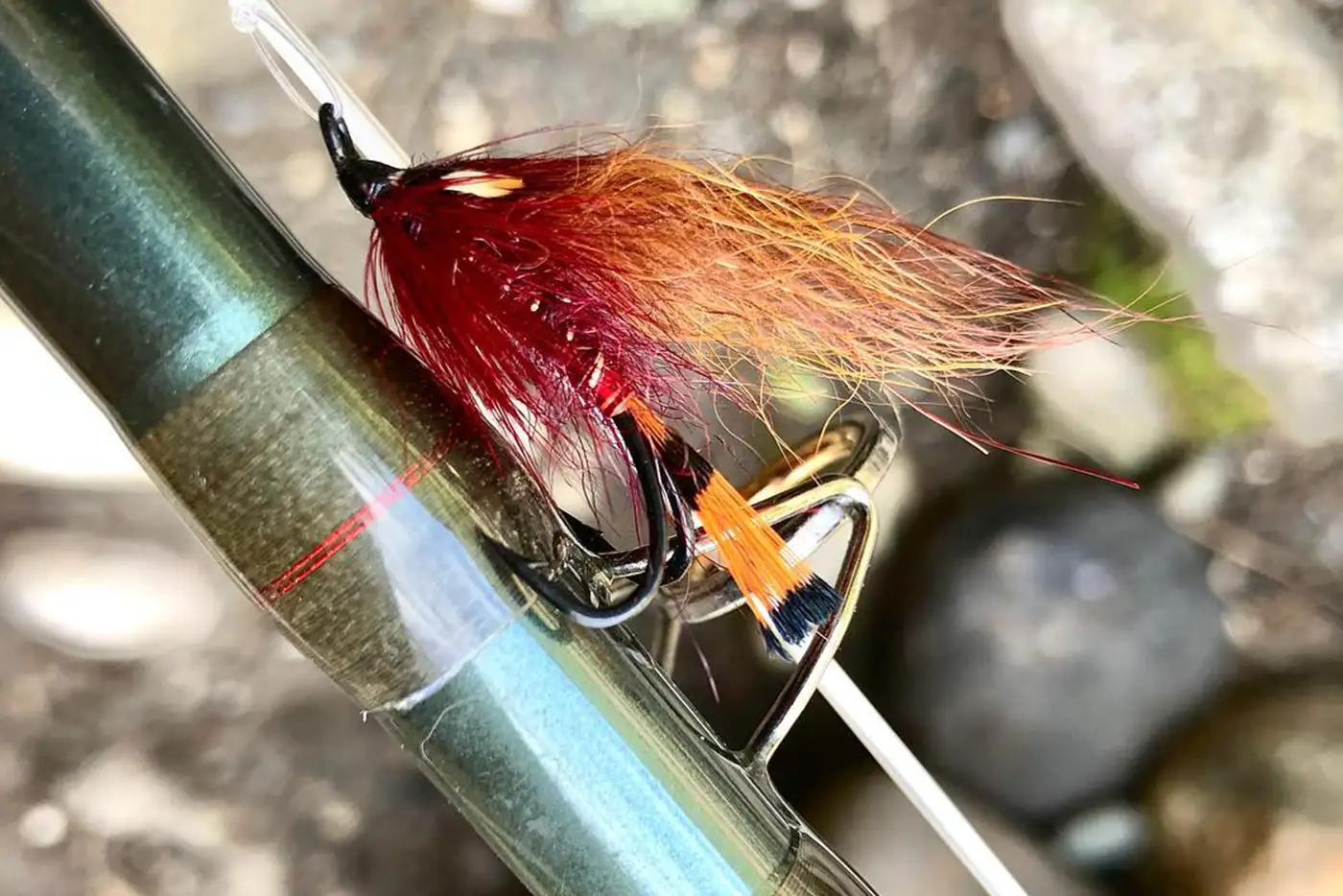 A fly fishing rod with a red and orange fly attached to it.