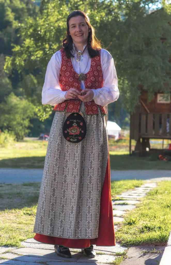 A woman in a traditional dress standing in front of a house. 

Keywords added: Traditional dress